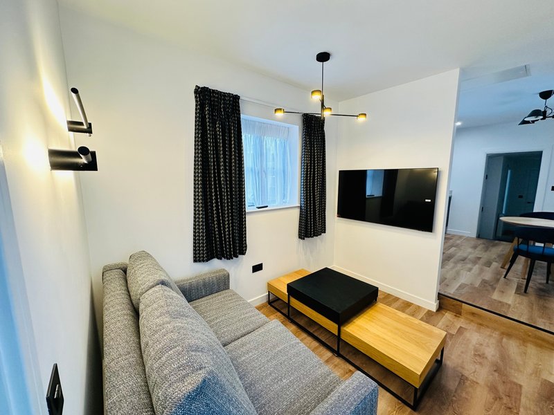 Modern living room with gray sofa, wall-mounted TV, black curtains, and wooden floor