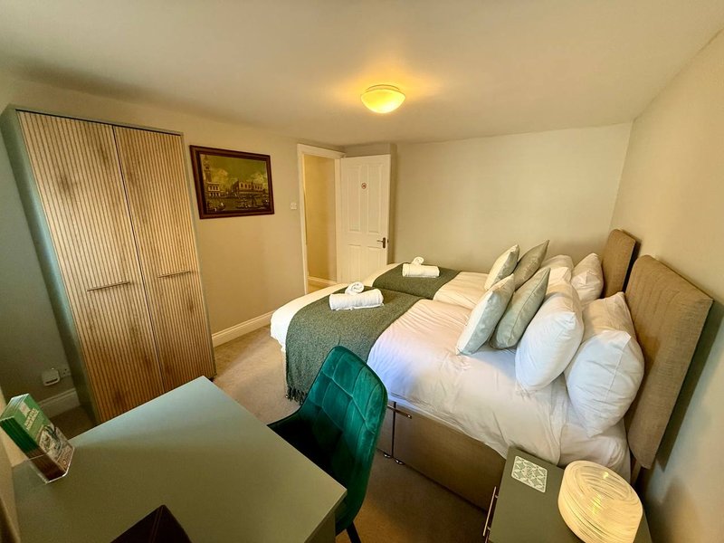 Bedroom with double bed, multiple pillows, wooden wardrobe, desk chair and ceiling light