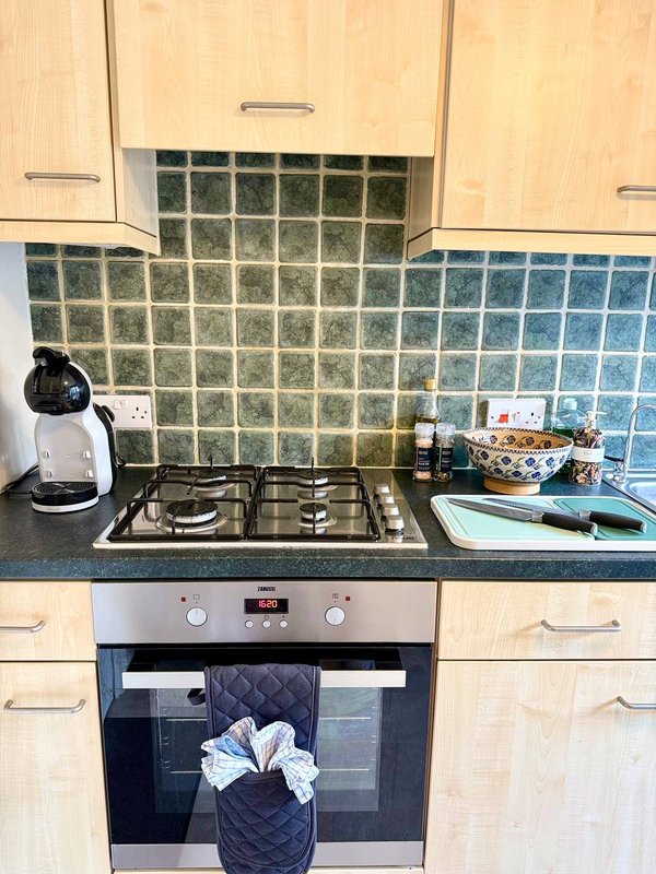 Kitchen with gas hob, built-in oven, green tile splashback and wood cabinets