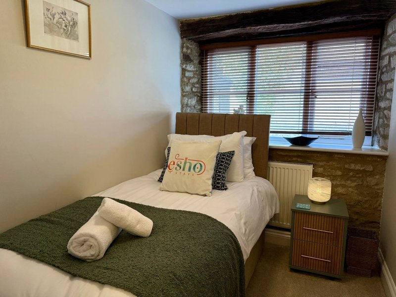 Bedroom with single bed, green throw, rolled towels, wooden headboard and bedside table