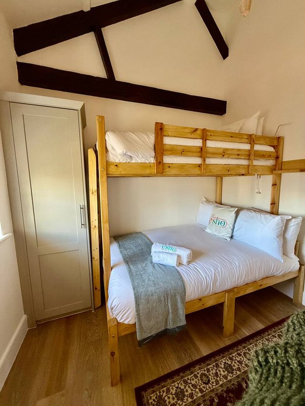Bedroom with wooden bunk bed, white bedding, grey throw, exposed beams, and wooden floor