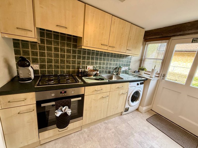 Kitchen with light wood cabinets, black countertop, gas hob, oven and washing machine