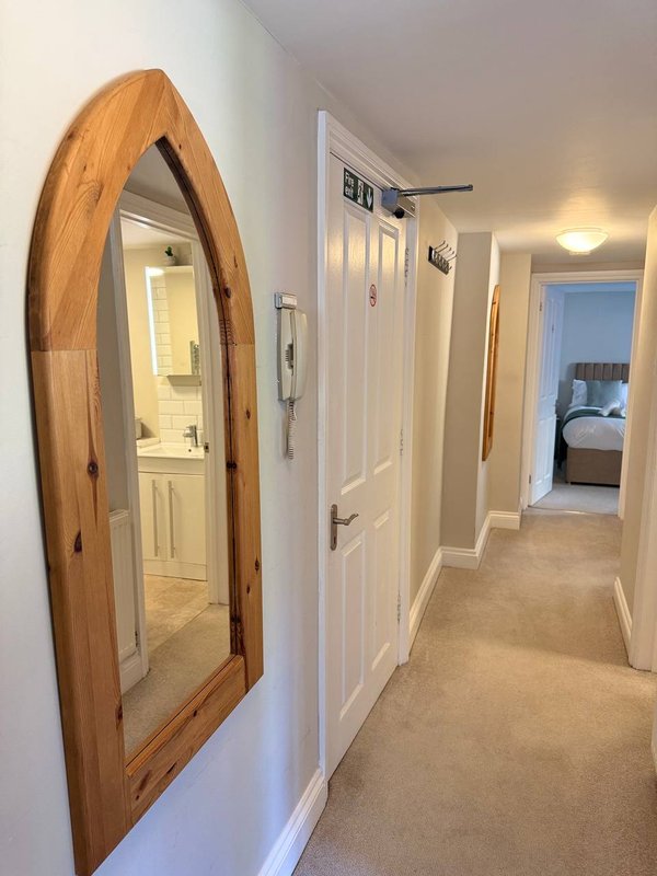 Hallway with wooden arched mirror, white doors, and carpet flooring leading to bedrooms
