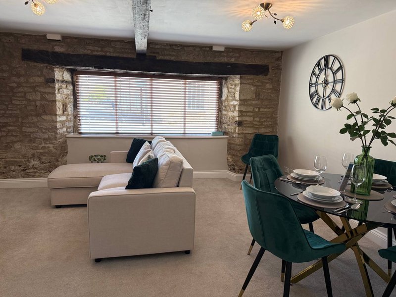 Open-plan living and dining area with cream sofa, dining table, green chair, and brick feature wall