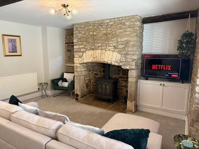 Living room with cream sofa, stone fireplace with wood stove, television, and ceiling light fixture