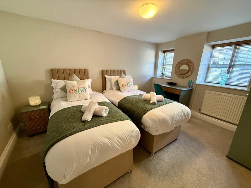 Twin bedroom with beige upholstered headboards, green bedding, white pillows and decorative cushions