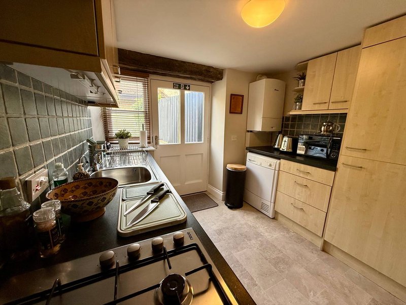 Compact kitchen with light wood cabinets, gas hob, sink, and small dining area