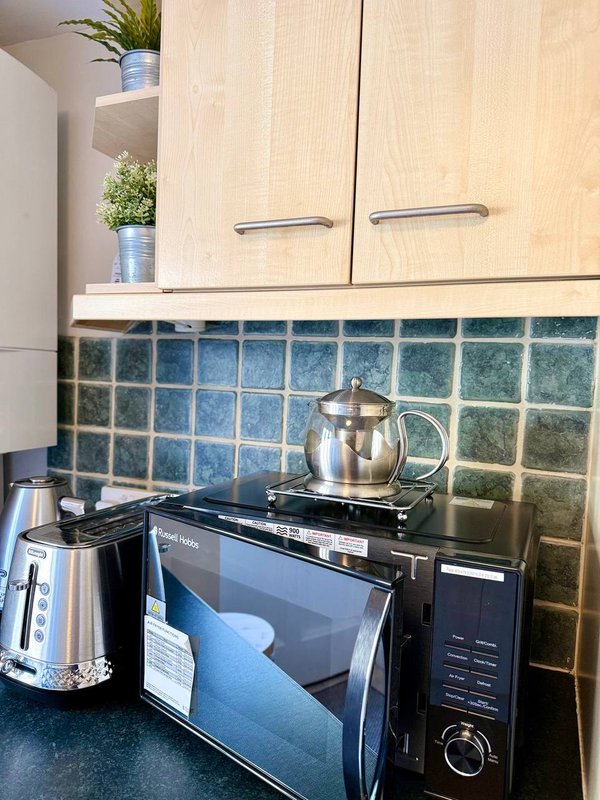 Kitchen corner with cream cabinets, blue tile backsplash, microwave, kettle and metal teapot