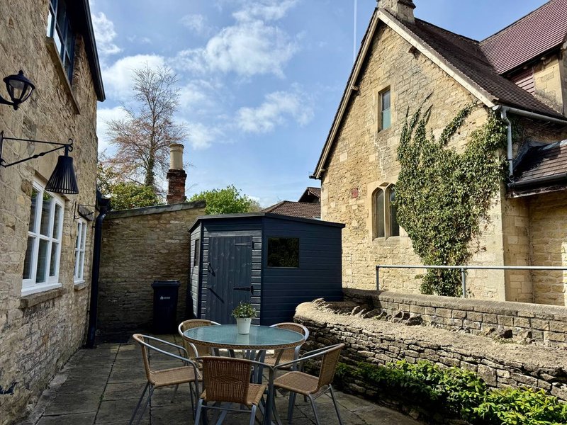 Stone cottage exterior with patio seating area, garden shed and ivy-covered wall