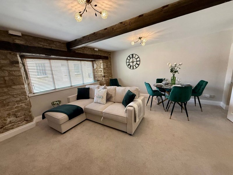 Open-plan living area with cream sofa, dining table, exposed wooden beams and wall clock