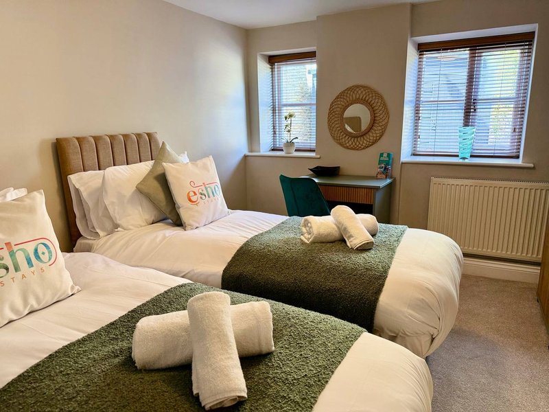 Bedroom with two single beds, green throws, white pillows and rolled towels