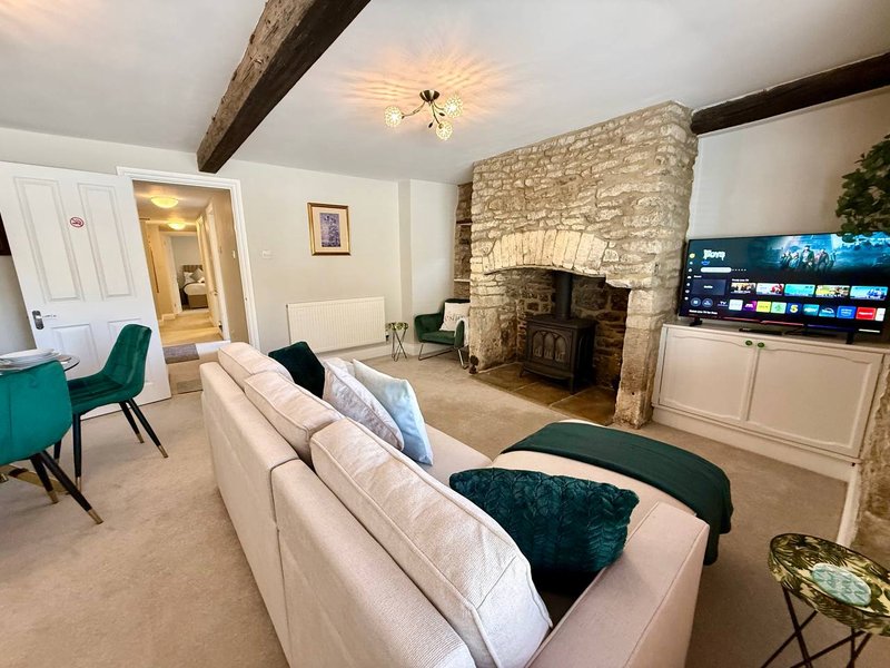 Living room with cream sofa, stone fireplace, wood beams, TV, and teal armchair