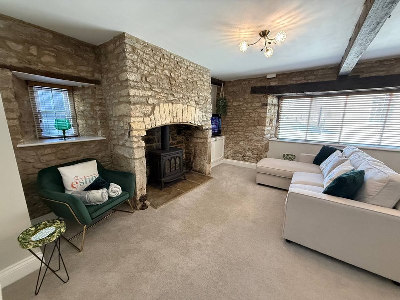 Stone fireplace living room with wood-burning stove, cream sofa, green armchair and windows