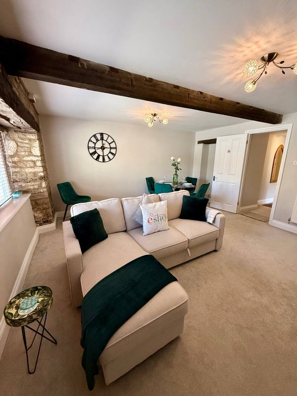 Living room with cream sofa, dark green cushions, exposed beam ceiling, wall clock and side table