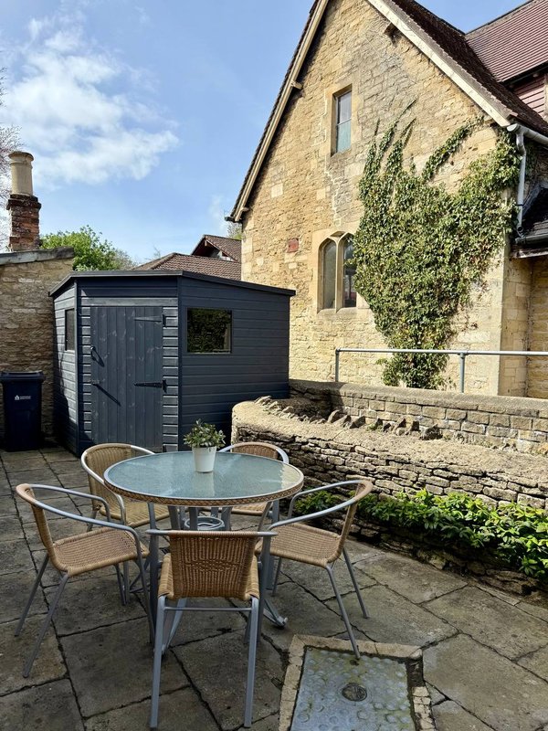Stone cottage exterior with patio seating area, garden shed and ivy-covered walls