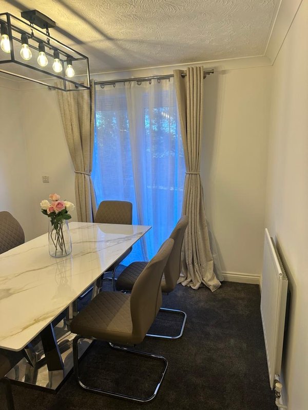 Dining room with white table, grey chairs, flowers in vase, and floor-to-ceiling curtains
