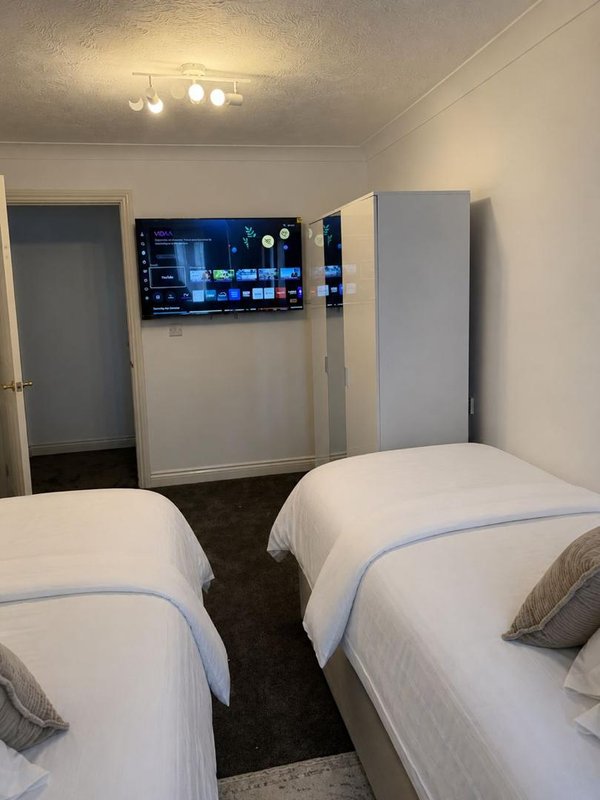 Twin bedroom with two white beds, wall-mounted TV, ceiling lights and grey door