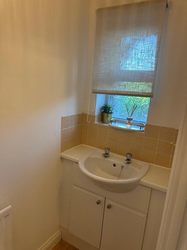 Bathroom with white pedestal sink, beige tile splashback, window with blind and potted plant