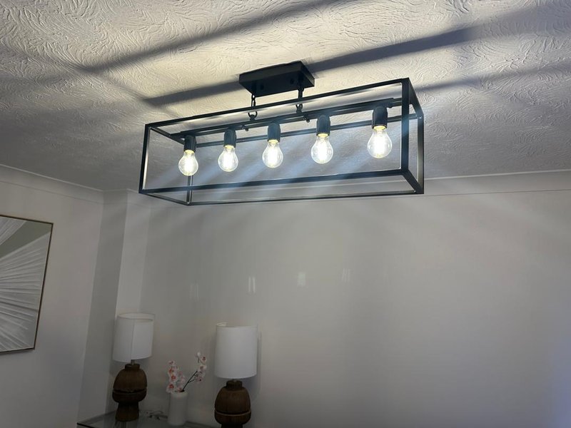 Ceiling light fixture with five bulbs in black metal frame above white walls