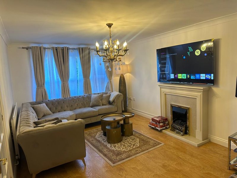 Elegant living room with grey sofa, fireplace, mounted TV, chandelier and large windows