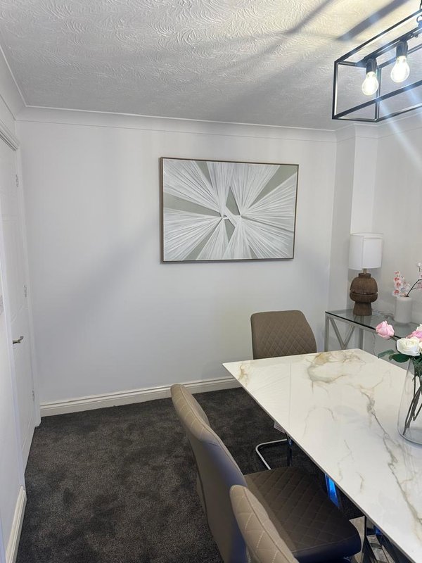 Modern office or study room with white walls, framed abstract artwork, marble-top desk, upholstered chairs, and dark carpet flooring