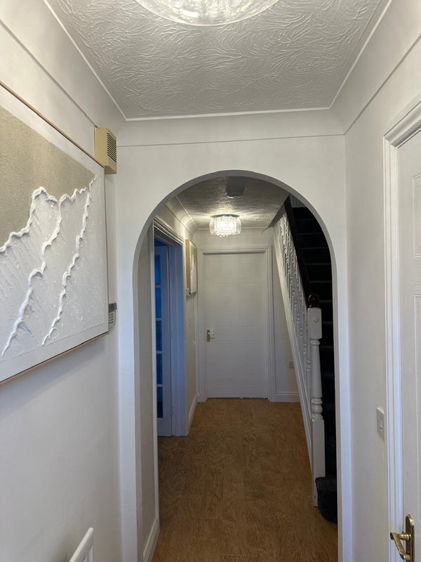 Hallway with arched doorway, white walls, cork flooring and ceiling light