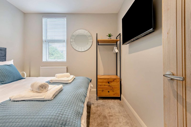 Modern bedroom with double bed, wall-mounted TV, window with blinds, and wooden storage rack