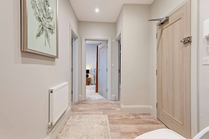 Bright hallway with light wood flooring, cream walls, framed botanical artwork, and pale wooden doors