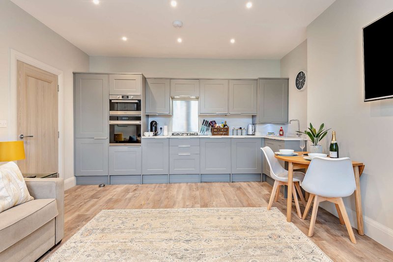 Open-plan kitchen and living area with grey cabinetry, wooden flooring, and dining table