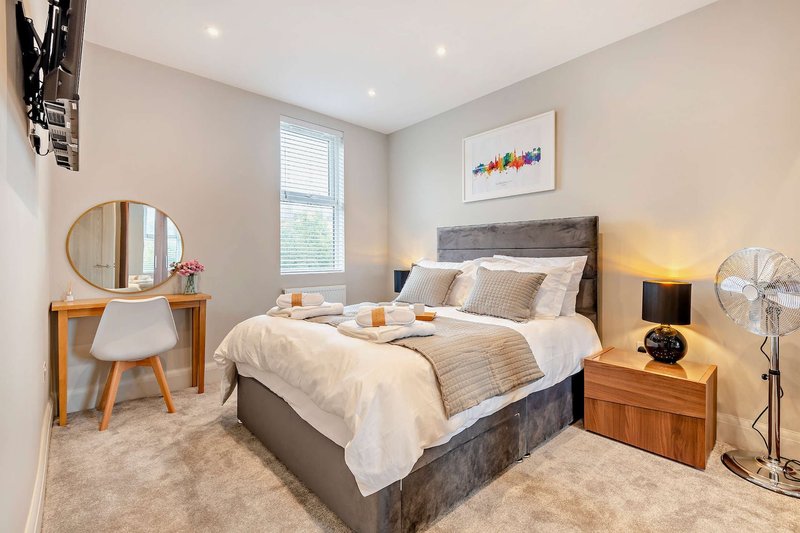 Modern bedroom with grey upholstered bed, wooden furniture, round mirror and window