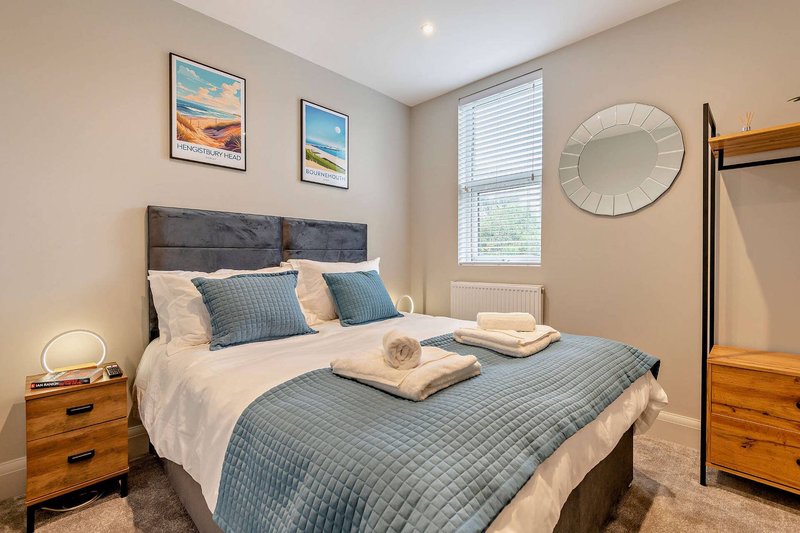 Bedroom with double bed, blue bedding, wooden nightstands, framed artwork, and round mirror