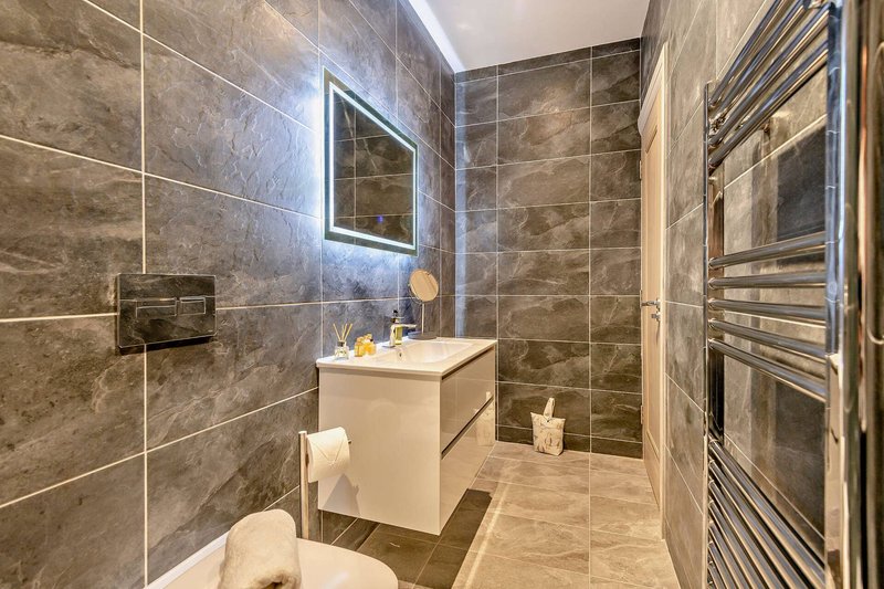 Modern bathroom with tiled walls, illuminated mirror, white vanity unit and heated towel rail