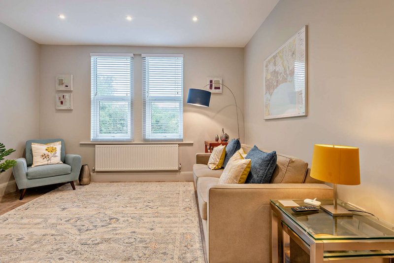 Spacious living room with beige sofa, armchair, windows, and modern lighting fixtures