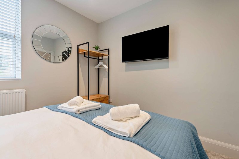 Bright bedroom with double bed, blue throw, wall-mounted TV, mirror and clothing rack