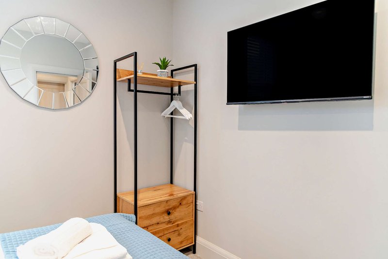 Bedroom corner with bed, round mirror, wooden shelving unit and wall-mounted TV