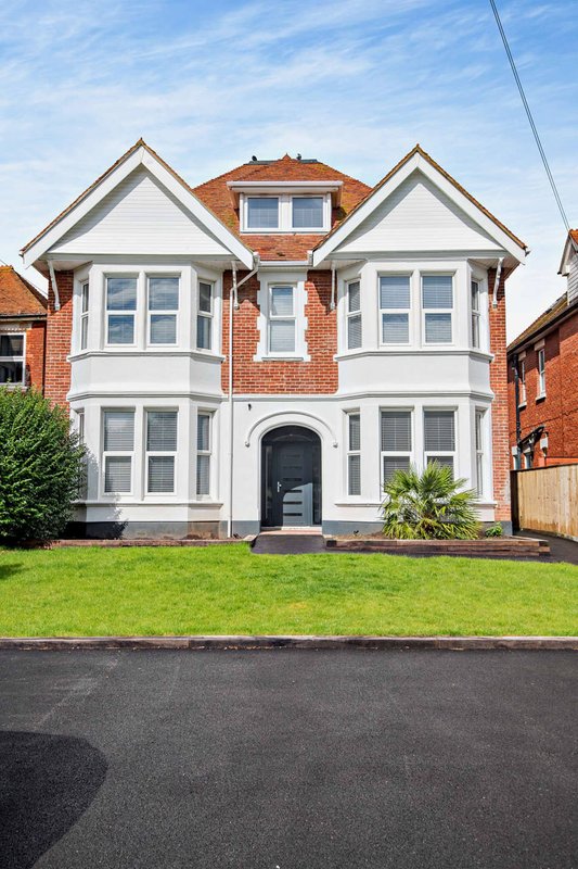 Two-storey brick house with white trim, bay windows, manicured front lawn and driveway
