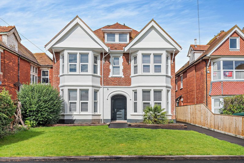 Brick and white detached house with manicured front lawn and driveway