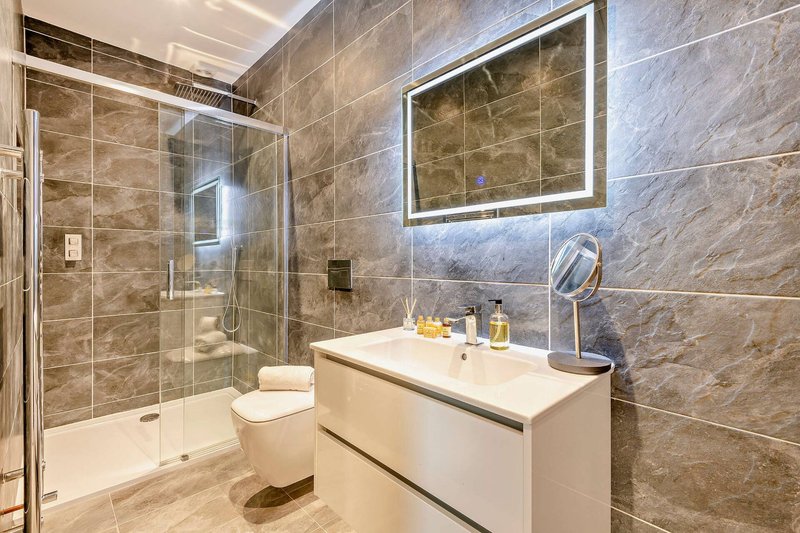 Modern bathroom with walk-in shower, vanity sink, illuminated mirror and tiled walls