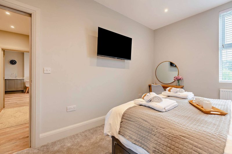 Modern bedroom with double bed, wall-mounted TV, round mirror, and open doorway to hallway