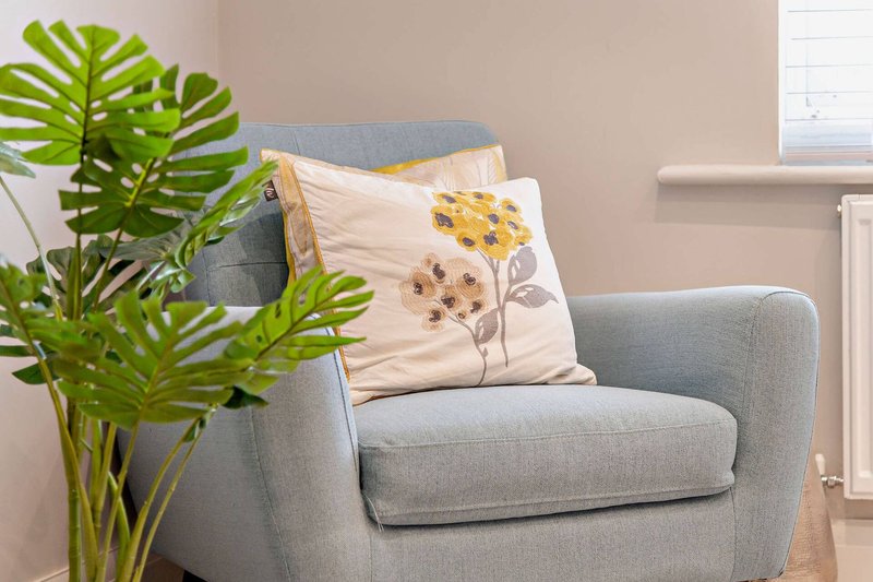 Gray upholstered armchair with floral cushion and potted plant beside window
