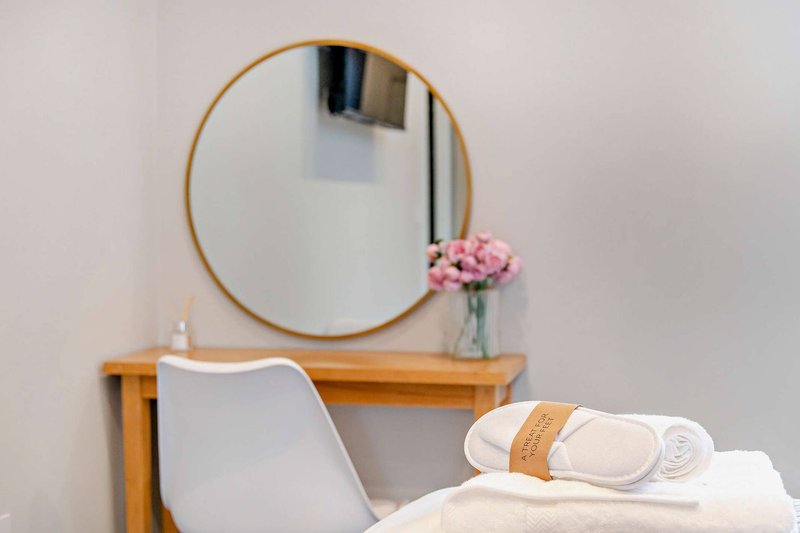 Bedroom corner with wooden desk, round mirror, white chair, and rolled towels