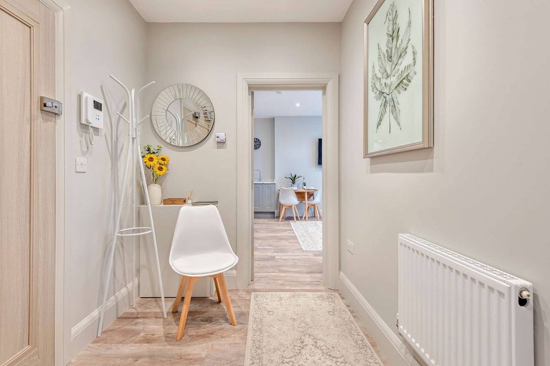 Bright hallway with white chair, decorative clock, yellow flowers, and view into living area