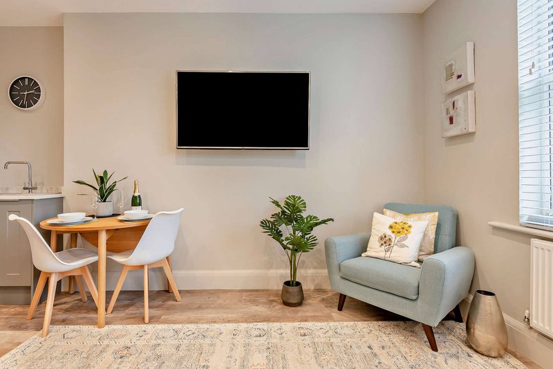 Modern living room with wall-mounted TV, wooden dining table, grey armchair and potted plants