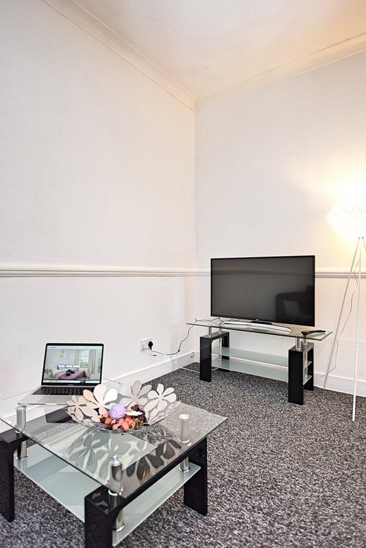 Modern living room with TV stand, glass coffee table, laptop, and grey carpet flooring