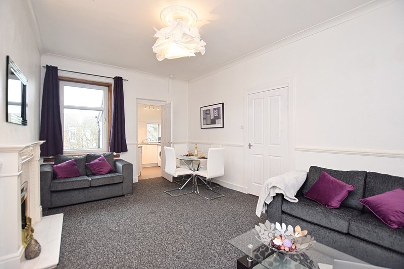 Bright living room with two grey sofas, purple cushions, fireplace and grey carpet