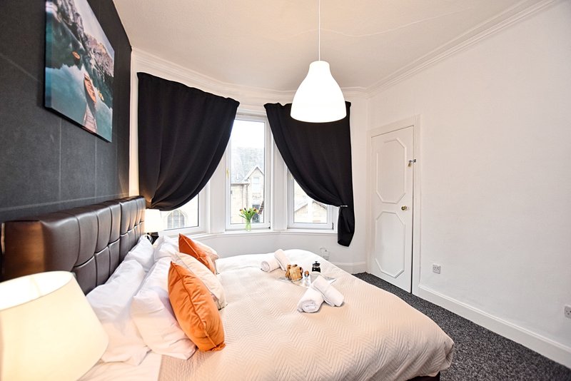 Modern bedroom with double bed, orange pillows, black curtains and pendant lighting