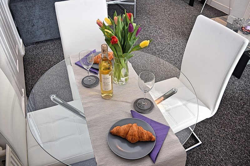 Dining table set with croissant, flowers, wine bottle, and place settings