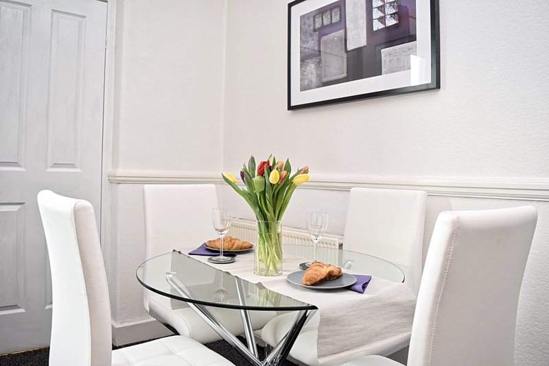 Modern dining area with round glass table, white chairs, and fresh tulips in vase
