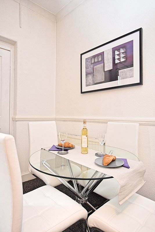 Dining area with round glass table, white chairs, and framed abstract wall art