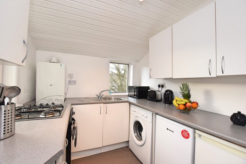 Modern kitchen with white cabinets, gas hob, washing machine, and counter fruit bowl